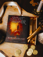 Elixir of Inner Light - Velvet Hammer - Book titled 'Velvet Hammer: Elixir of Inner Light' with gold packaging and coins on a dark surface.